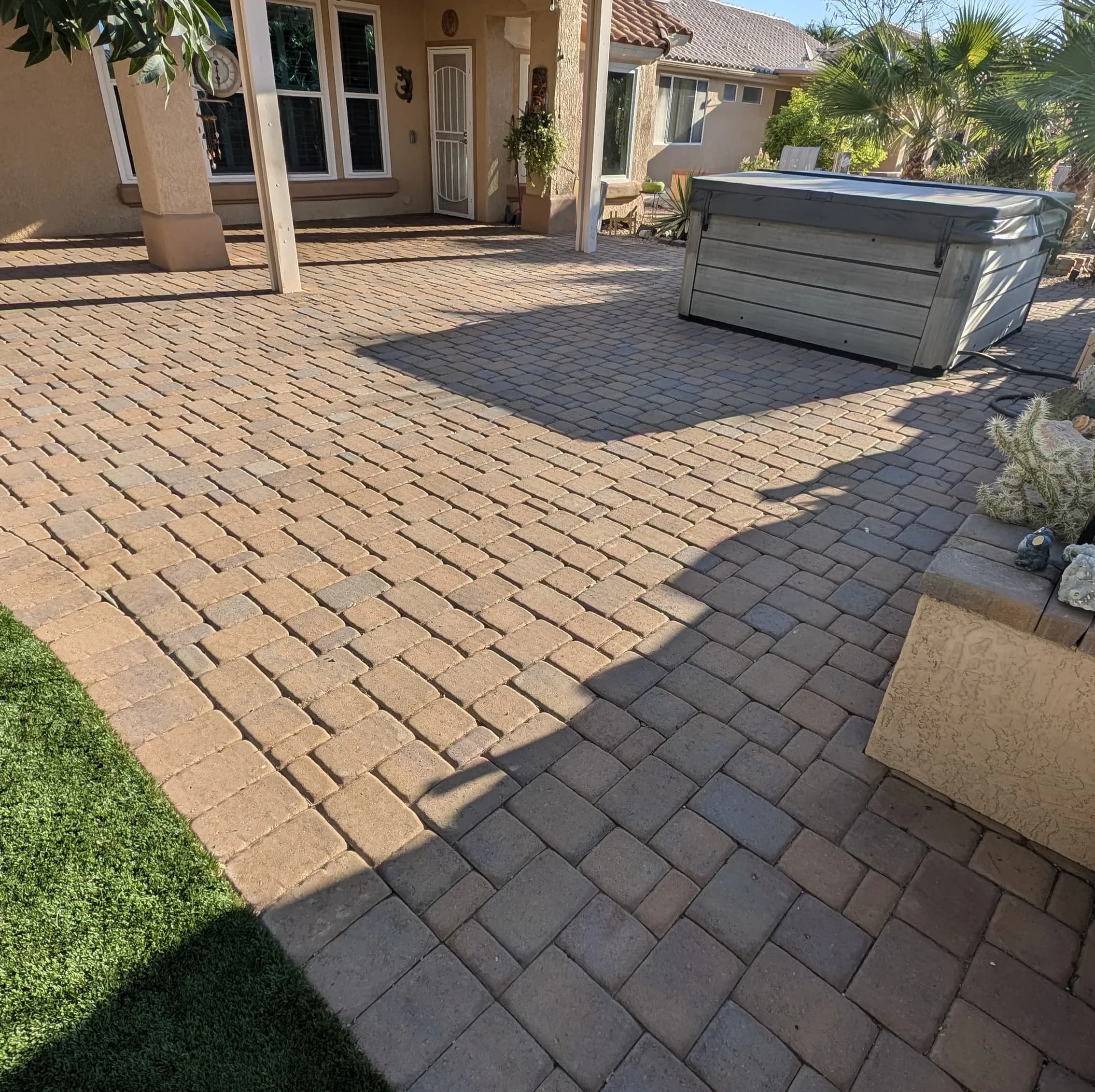 Paver patio with a hot tub, surrounded by palm trees and a well-maintained landscape.