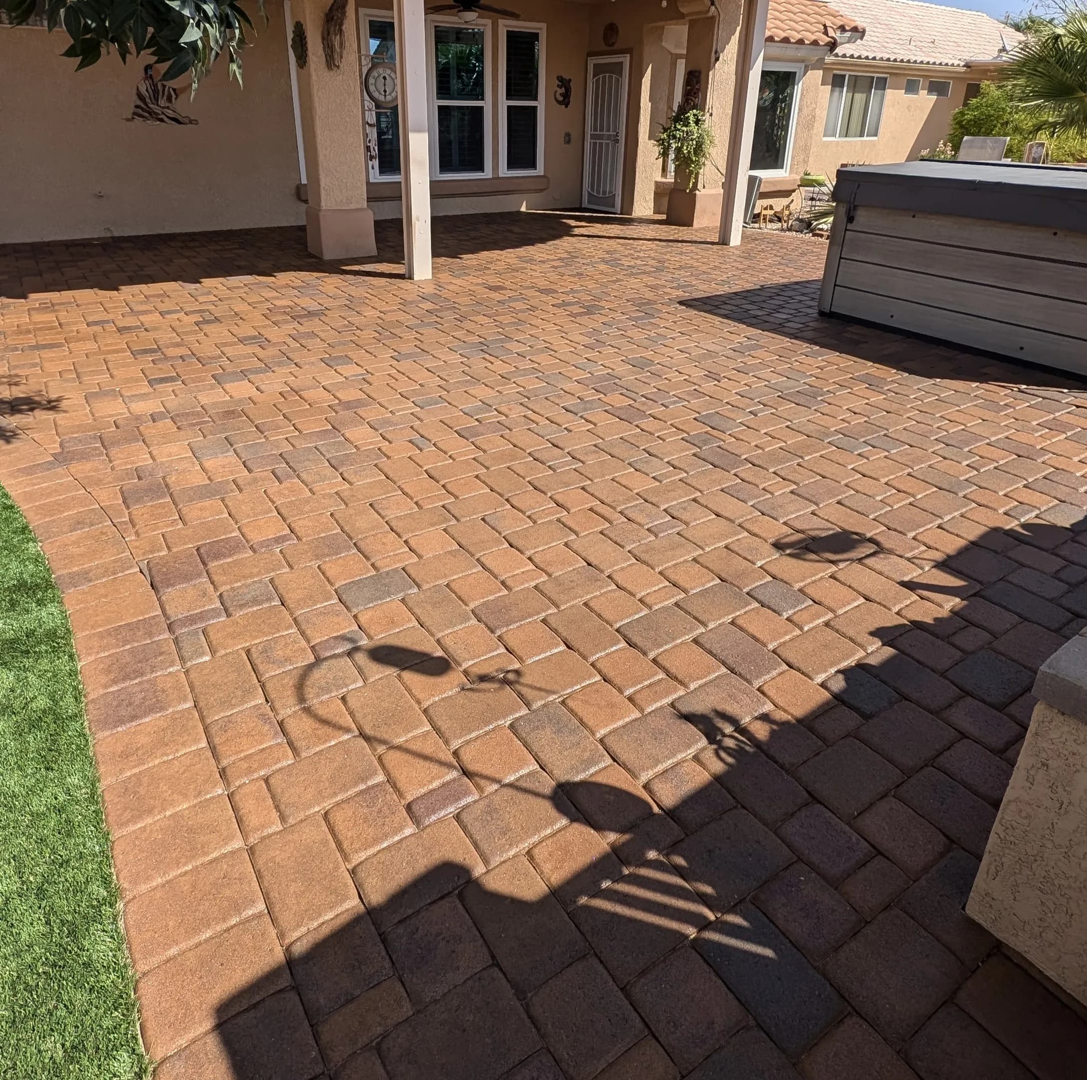 Paver patio with shaded seating area and outdoor hot tub in residential backyard.