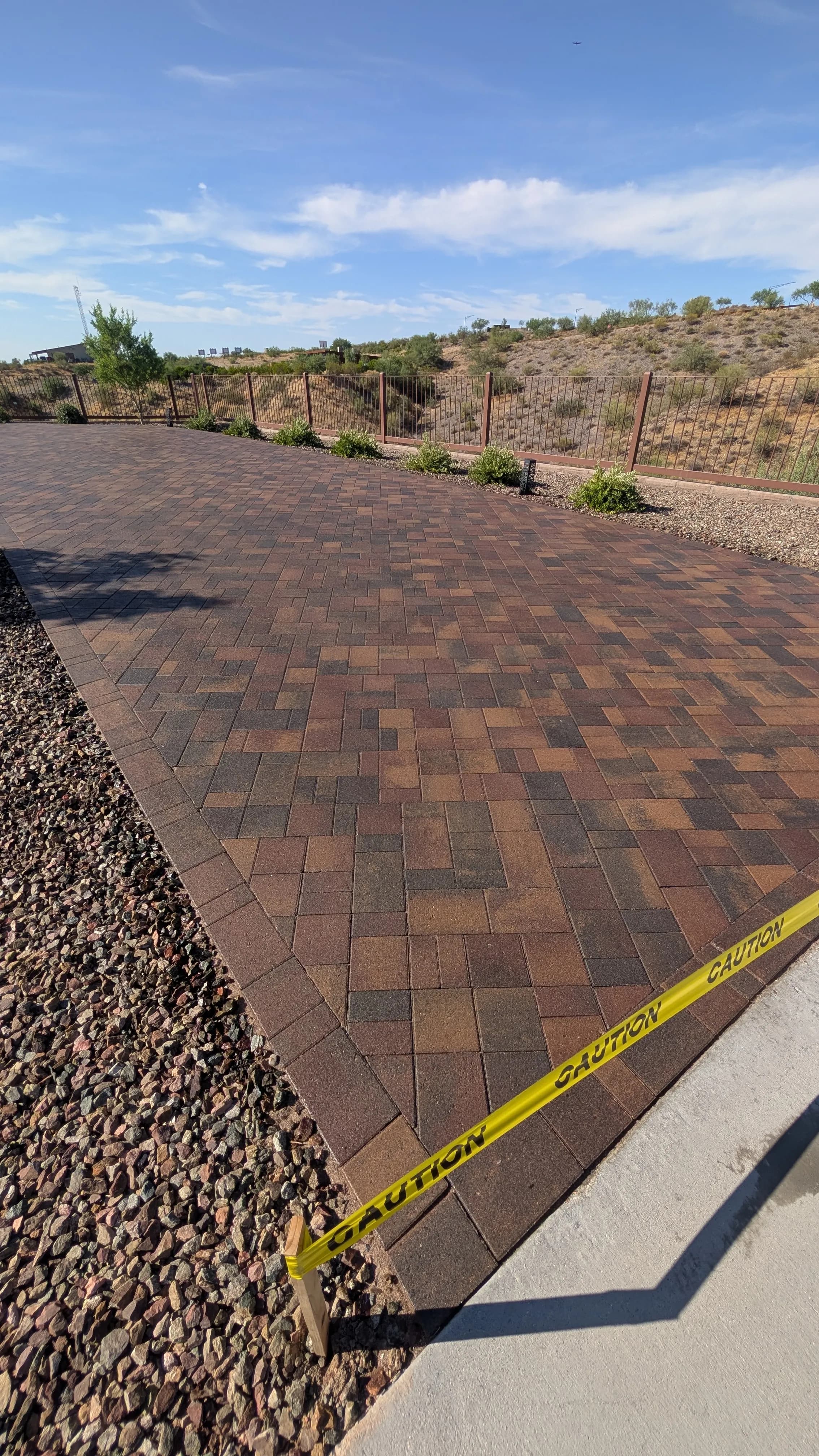 Newly installed paver patio with caution tape, surrounded by desert landscaping.