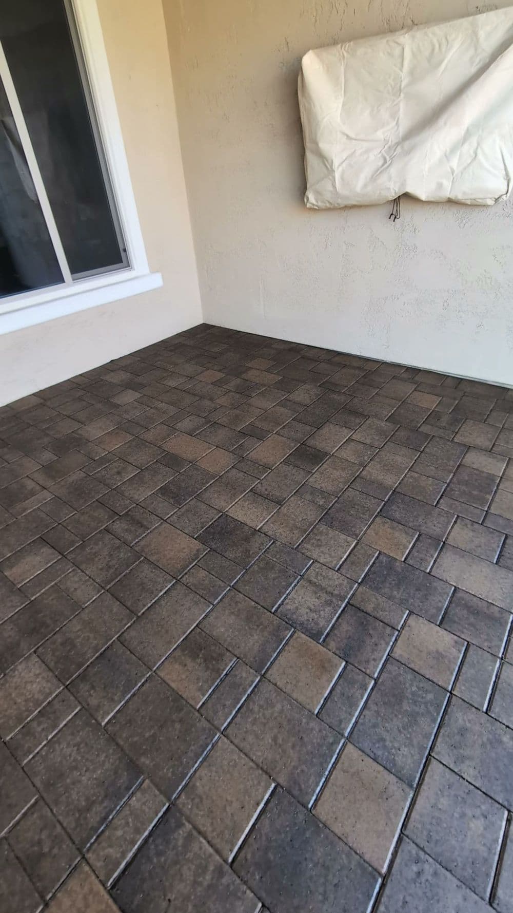 Paver patio with a natural stone finish and covered window on a light-colored wall.