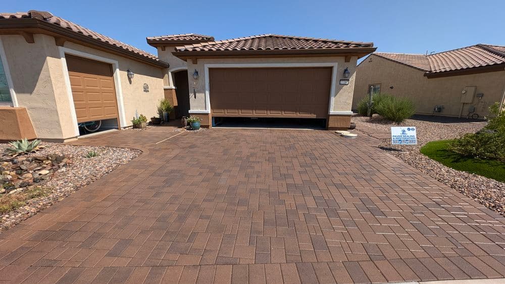 Stylish home exterior with a textured brick driveway and a tan garage door under a blue sky.
