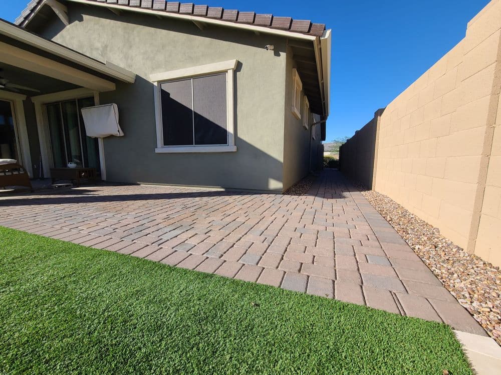 Patio area with paver stones, artificial grass, and a side walkway next to a house.