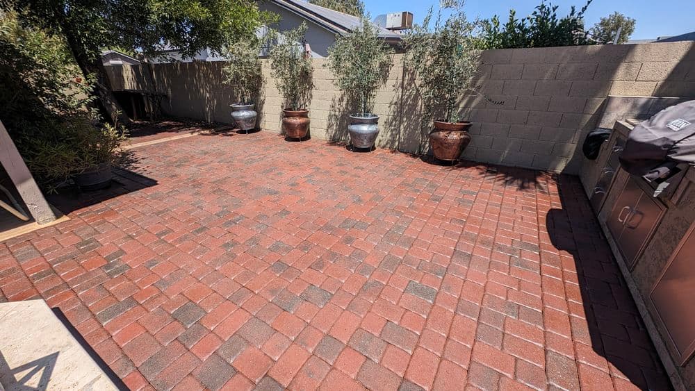 Paved outdoor patio with brick tiles and potted plants against a beige wall.