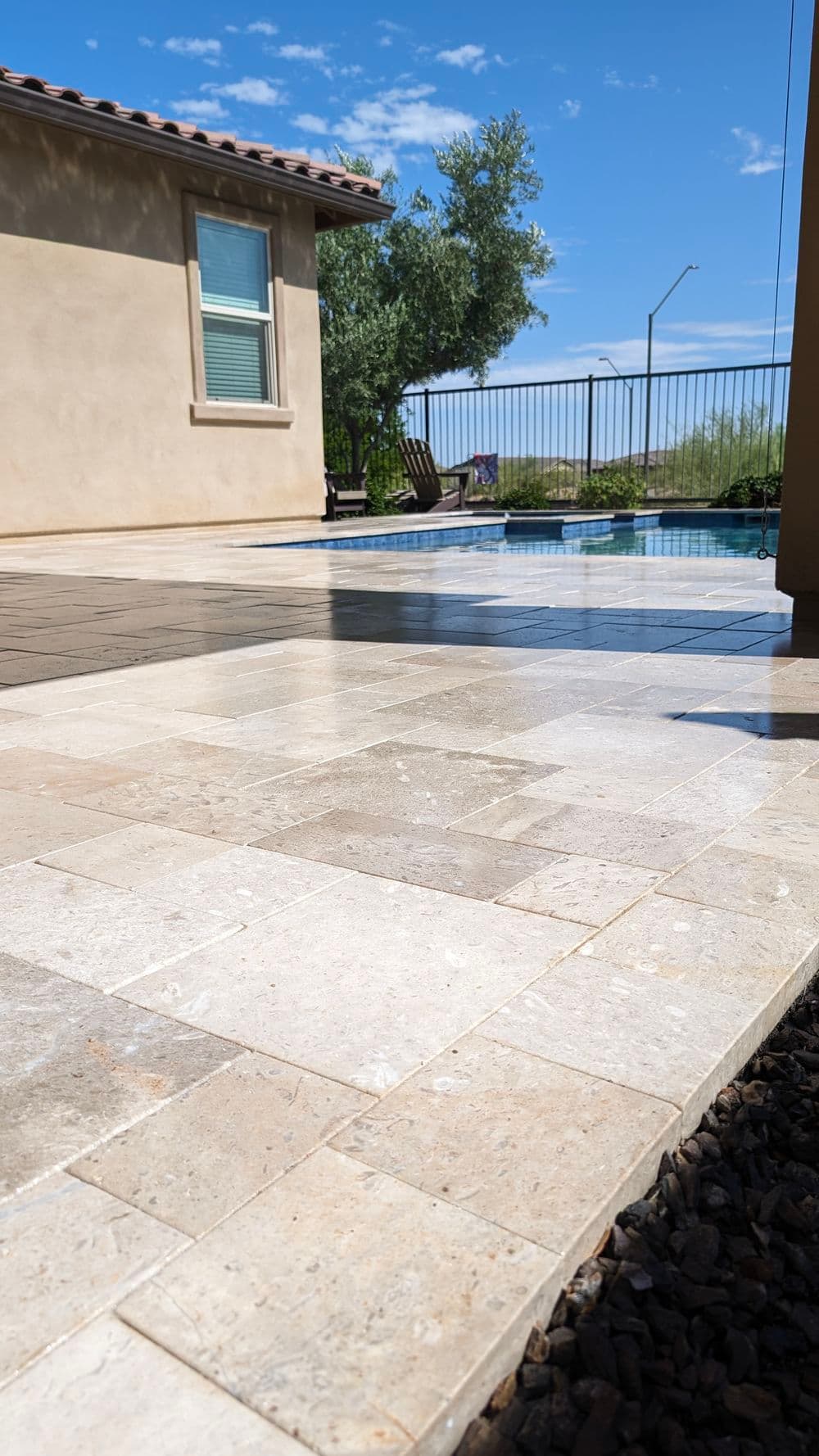 Elegant stone patio by poolside with clear blue sky and view of greenery nearby.