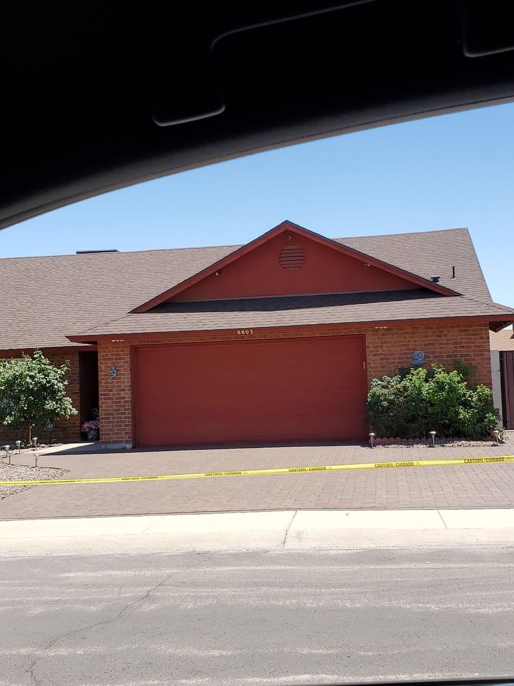 red brick house with garage door, landscaped yard, and caution tape in front