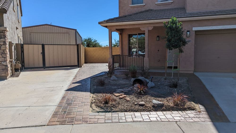 Modern desert landscape with paver walkway, yucca plants, and a garage in a residential setting.