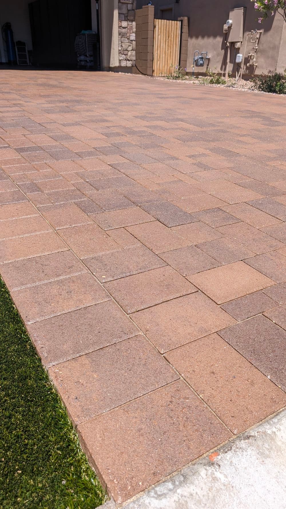 Paved driveway with brown interlocking pavers and green grass strip at the edge.