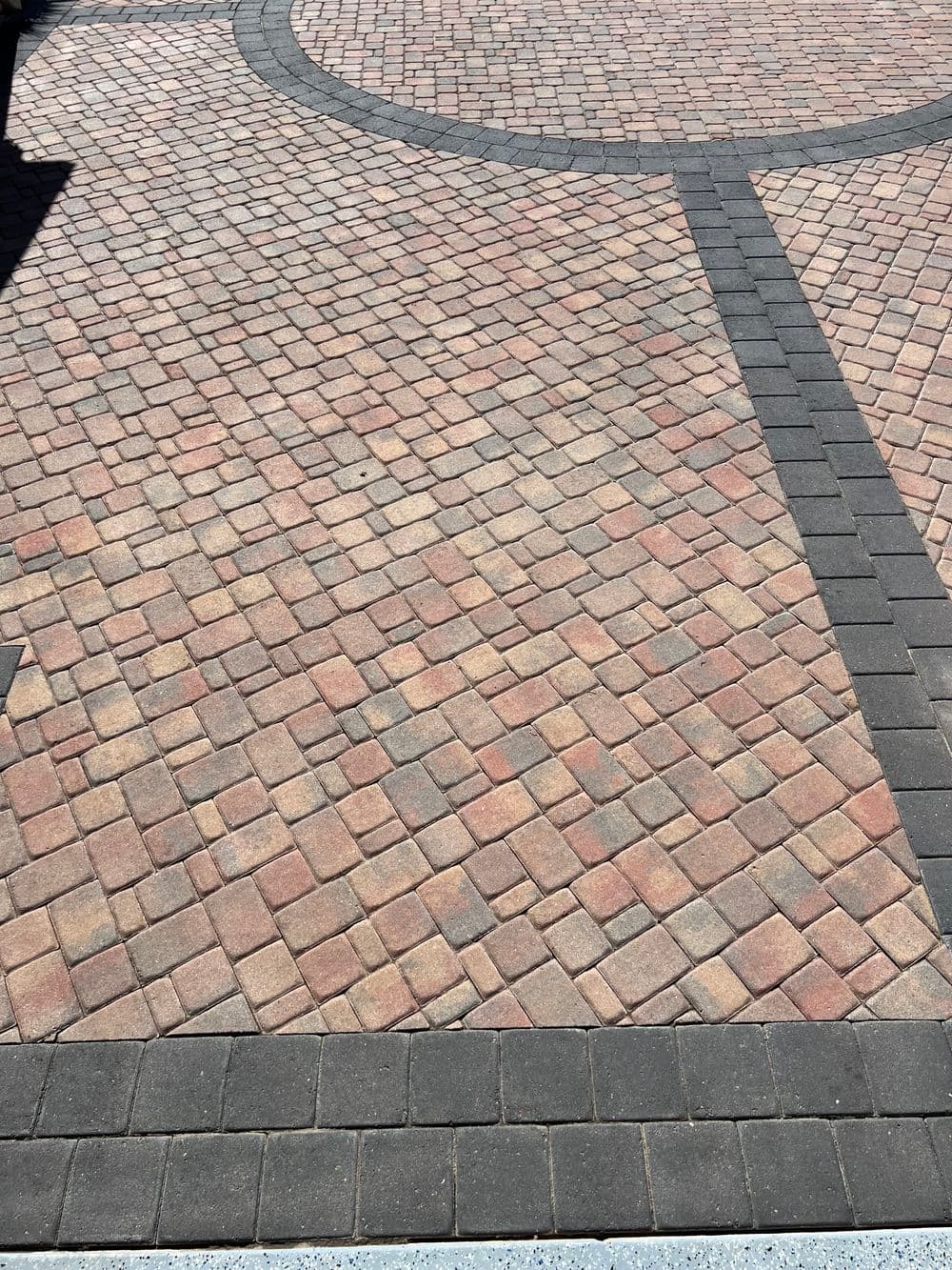 Paver stone walkway with intricate pattern of red and gray bricks.