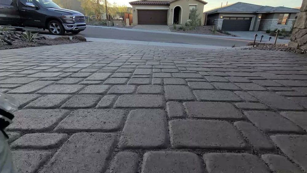 Paved driveway with cobblestone design, residential homes in the background.
