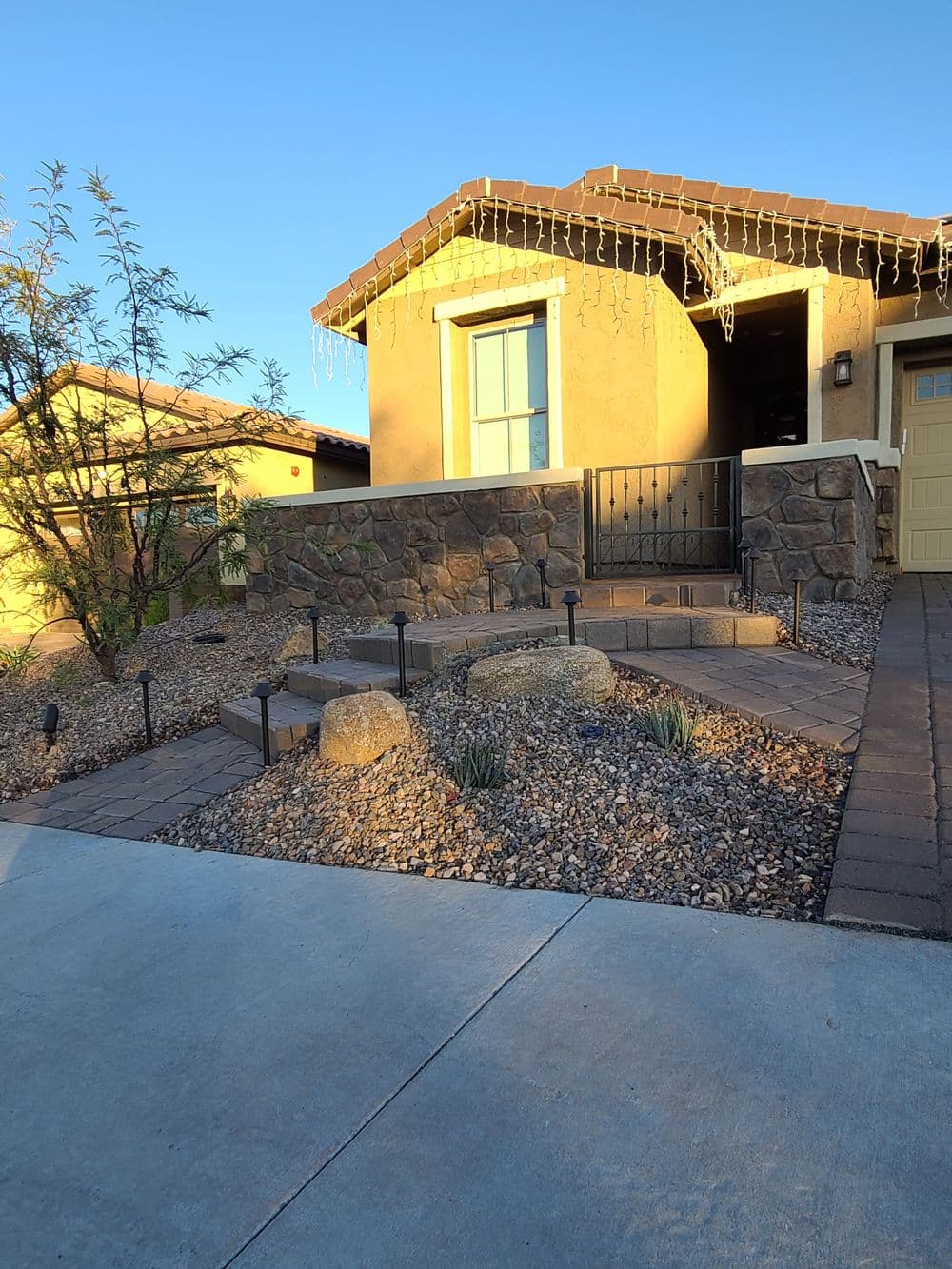 Desert-style home with stone accents, pathway, and decorative lights at sunset.