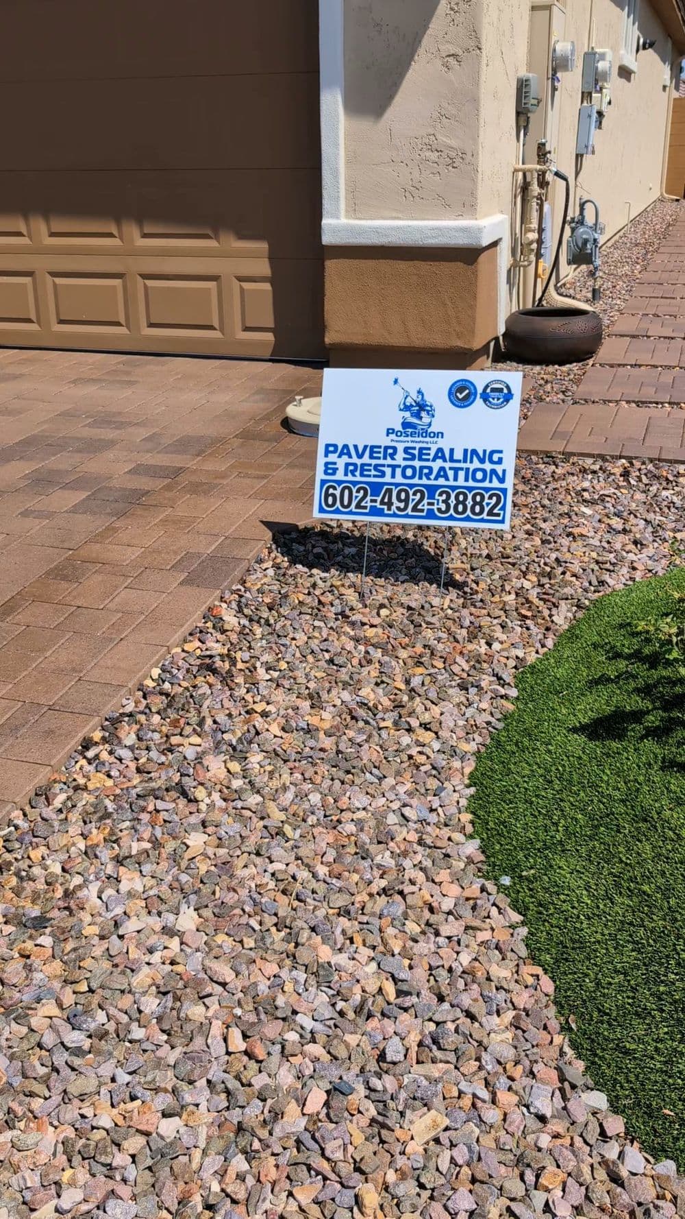 Paver sealing and restoration sign displayed in landscaped yard with decorative rocks.