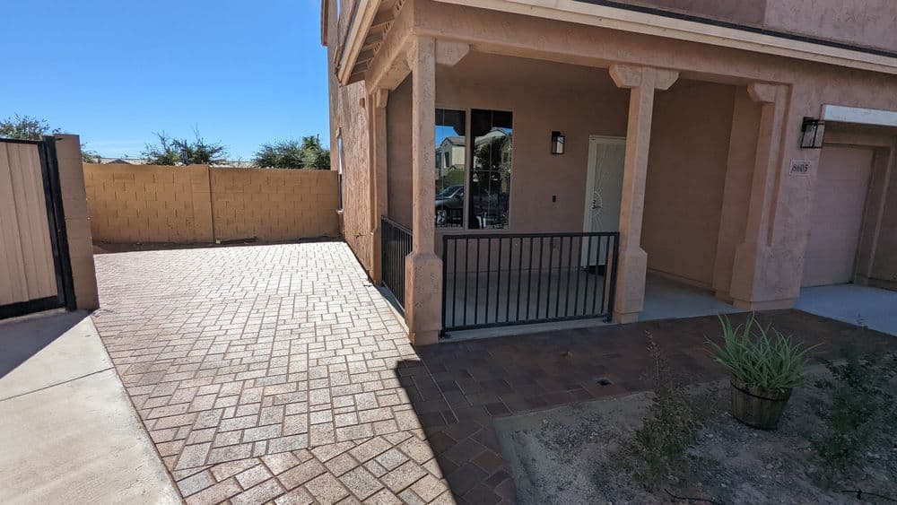 Exterior view of house entrance with paver driveway and decorative wall in sunny setting.