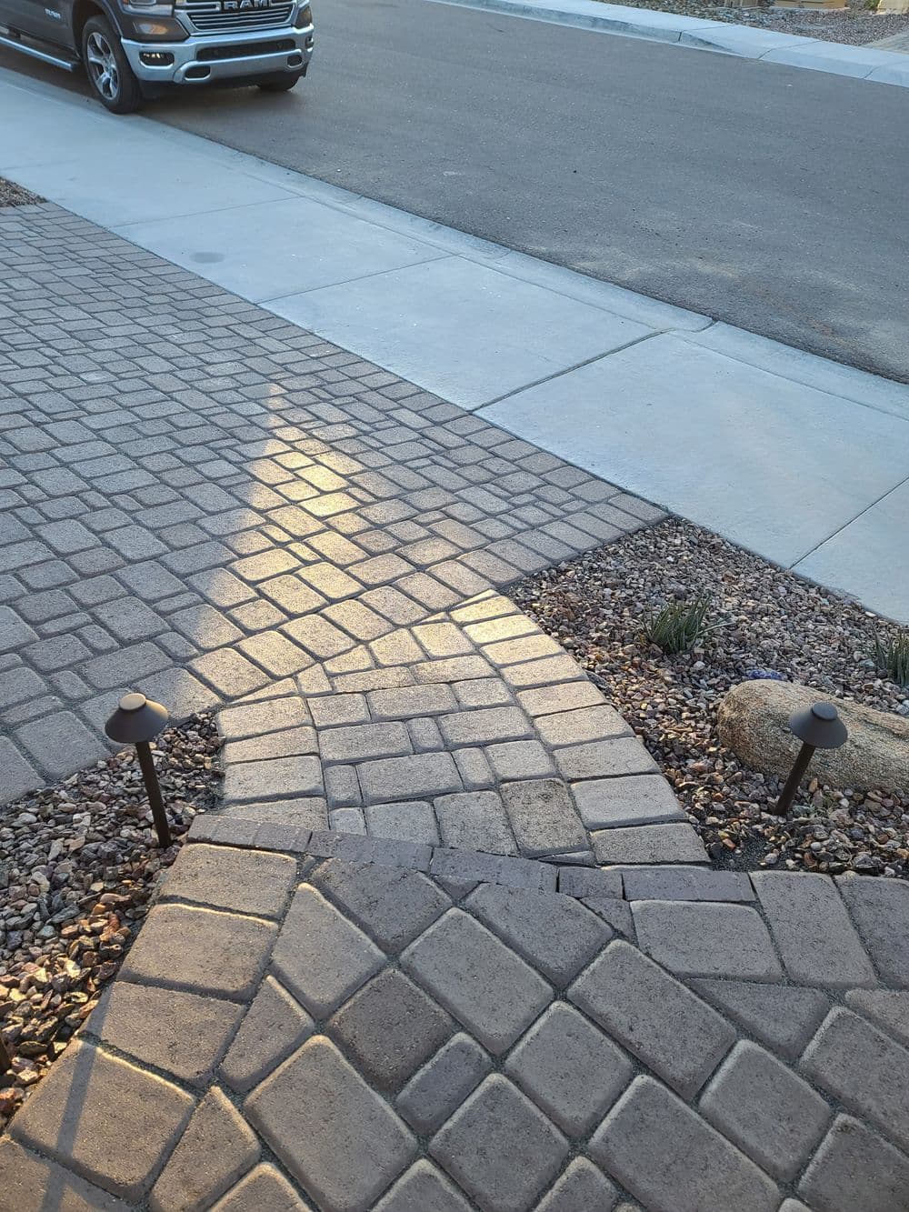 Paved walkway leading to driveway with decorative lights and gravel landscaping.