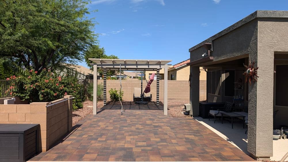 Patio with pergola and swings, surrounded by desert landscaping and blue sky.