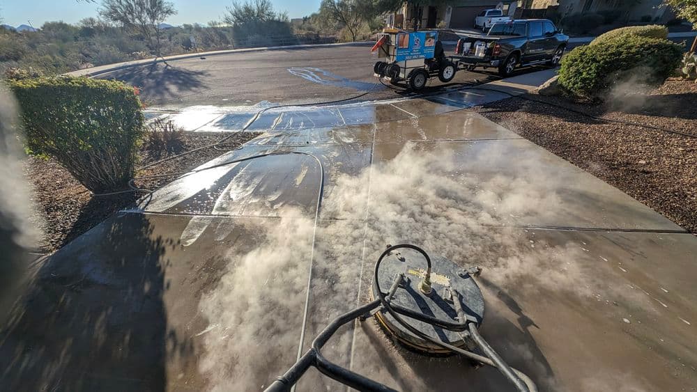 High-pressure steam cleaning of a driveway with visible steam and residential background.