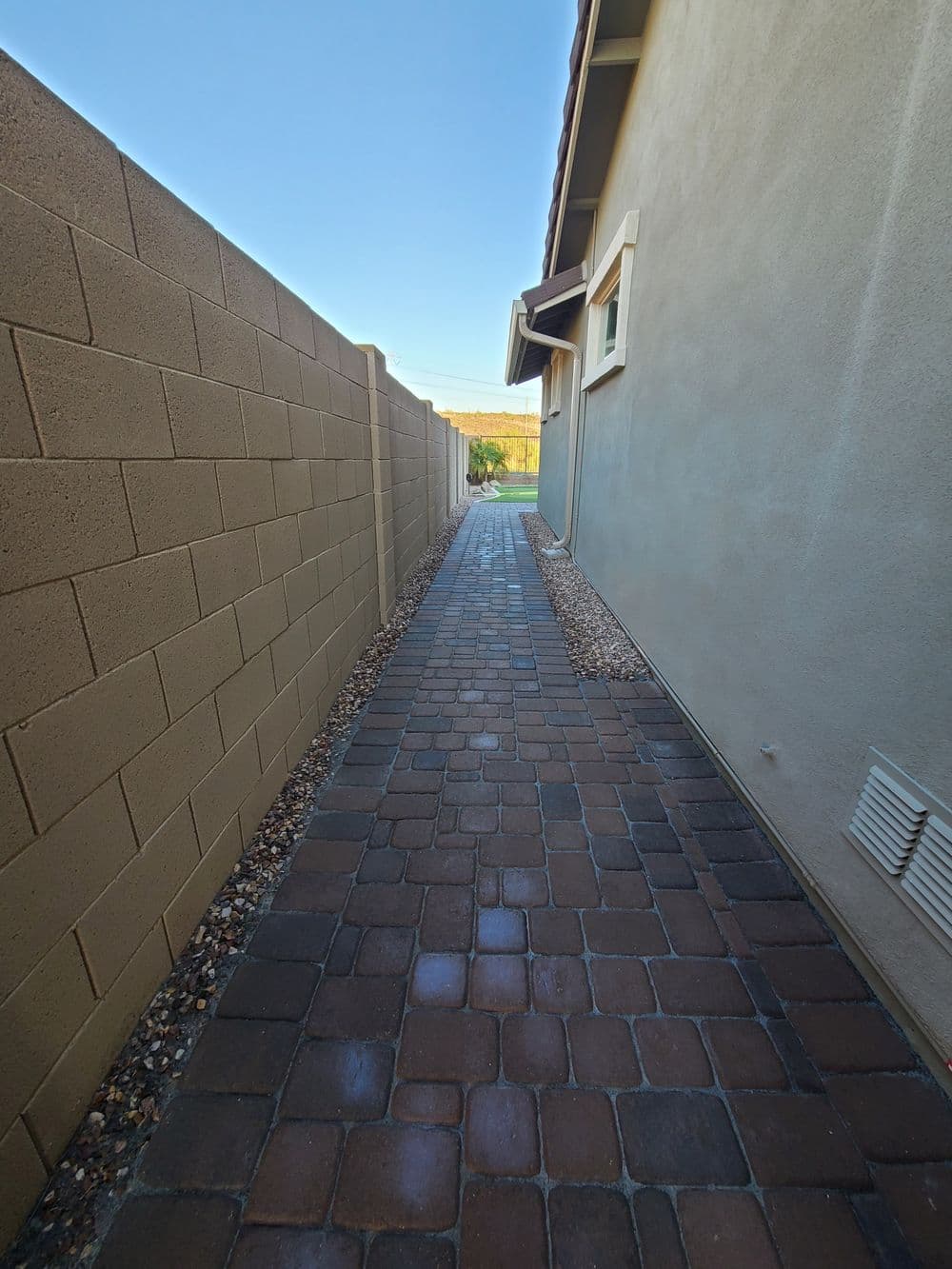 Narrow paved walkway between two walls, leading to a green outdoor space.