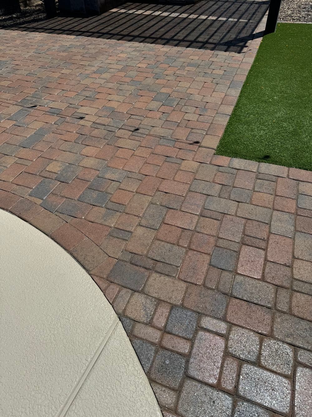Paved patio with various colored brick patterns and green artificial grass.