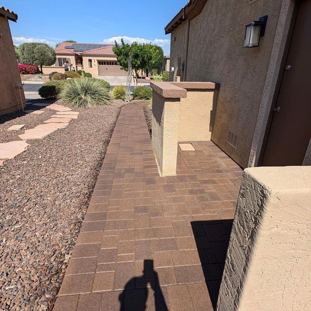 Brick pathway leading to a house with landscaping and clear blue sky.